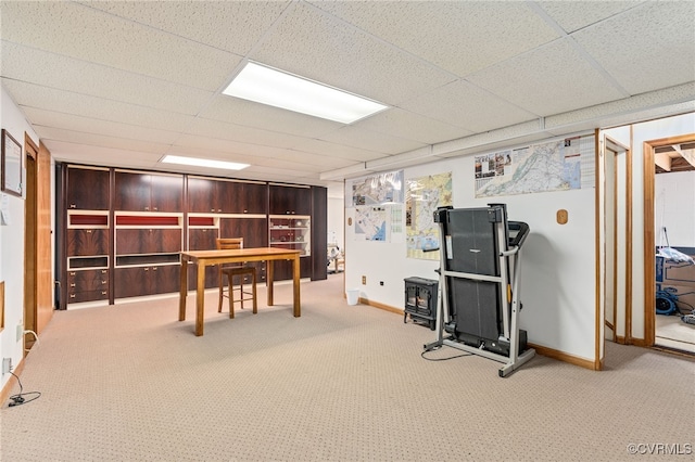 carpeted office space featuring a wood stove and a drop ceiling