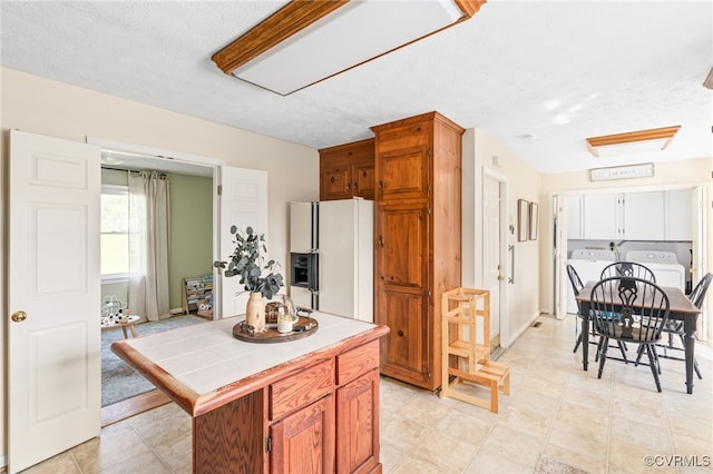 kitchen with tile countertops, white refrigerator with ice dispenser, separate washer and dryer, white cabinetry, and a textured ceiling