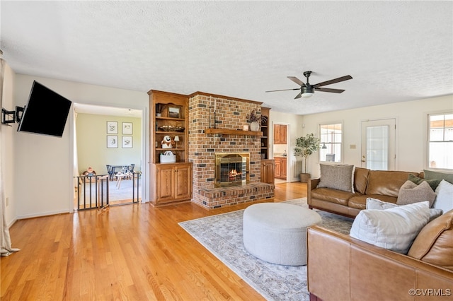 living room with a fireplace, a textured ceiling, light wood-type flooring, and ceiling fan