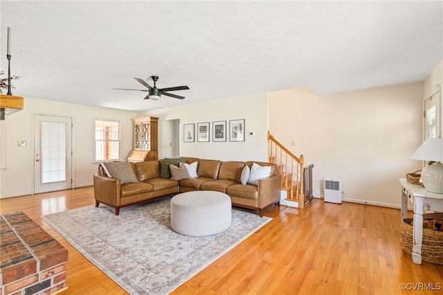 living room featuring a textured ceiling, light wood-type flooring, and ceiling fan