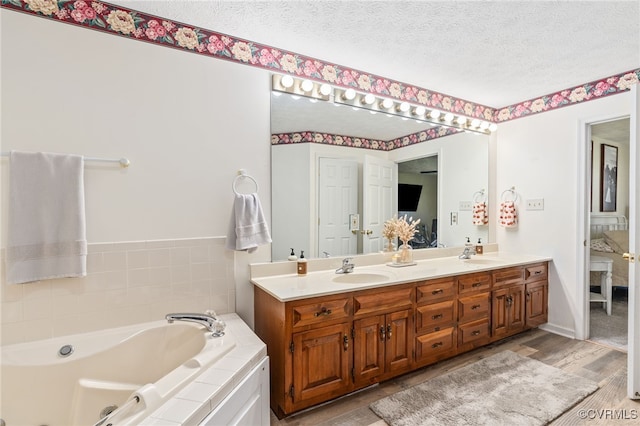 bathroom with vanity, a textured ceiling, hardwood / wood-style floors, and tiled bath