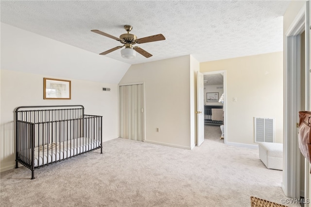 carpeted bedroom with lofted ceiling, a textured ceiling, a crib, and ceiling fan