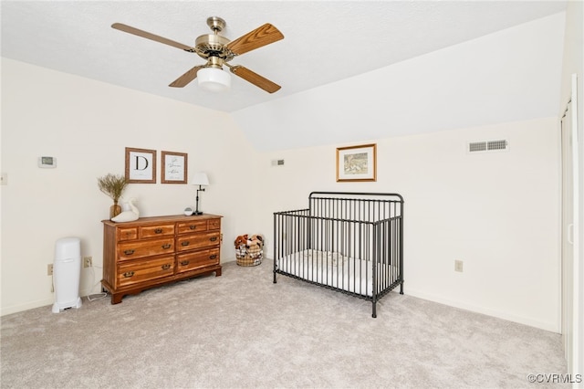 bedroom featuring ceiling fan, vaulted ceiling, light colored carpet, and a nursery area