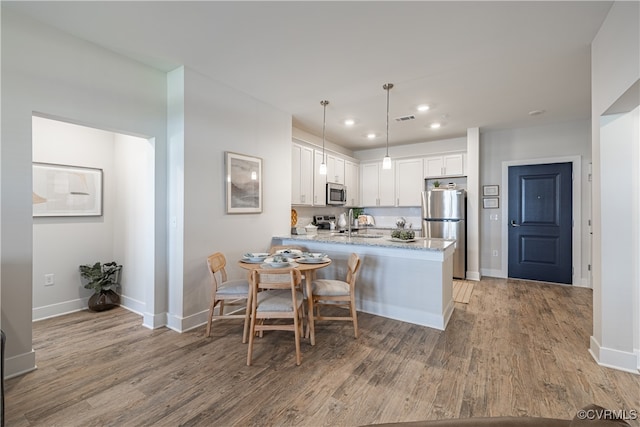 kitchen with light wood-type flooring, decorative light fixtures, stainless steel appliances, kitchen peninsula, and white cabinetry