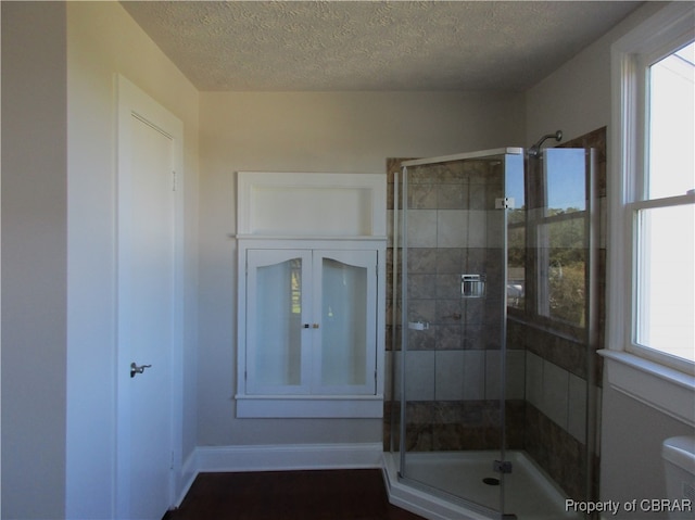 bathroom with plenty of natural light, a shower with door, toilet, and a textured ceiling