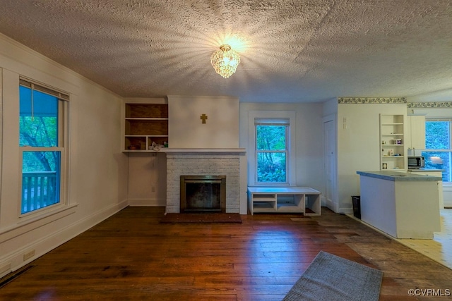 unfurnished living room featuring dark hardwood / wood-style floors, a stone fireplace, built in shelves, and a textured ceiling