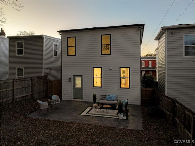 back house at dusk with outdoor lounge area and a patio area