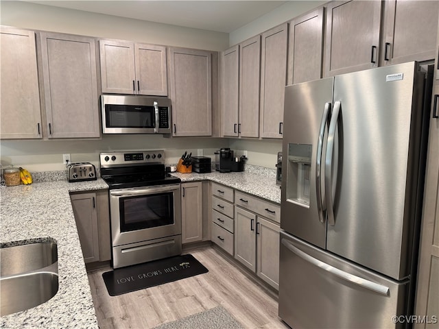 kitchen featuring light wood-type flooring, stainless steel appliances, light stone counters, and sink