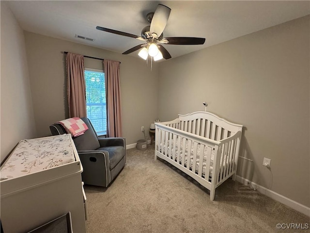 carpeted bedroom with a crib, baseboards, visible vents, and a ceiling fan