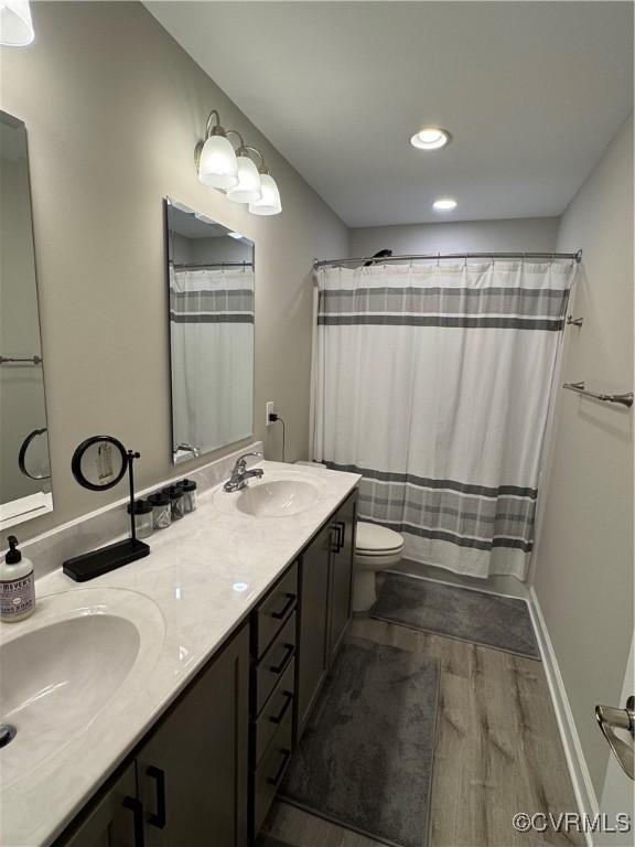 full bathroom featuring double vanity, a sink, toilet, and wood finished floors