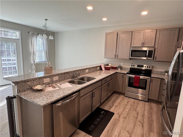 kitchen with light stone counters, a peninsula, a sink, appliances with stainless steel finishes, and light wood-type flooring