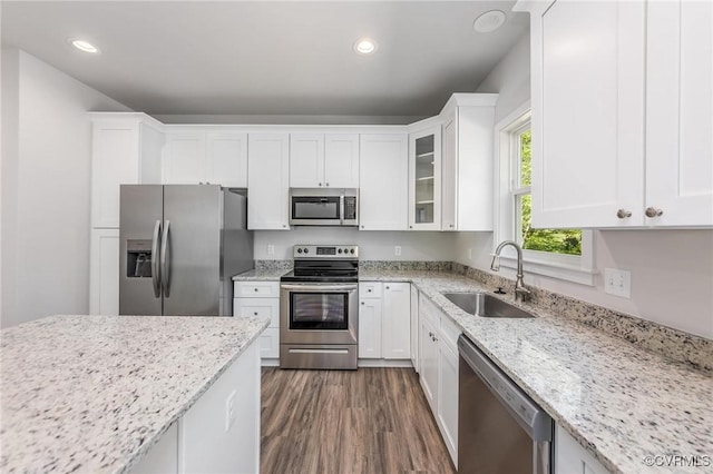 kitchen with stainless steel appliances, white cabinetry, sink, and light stone counters