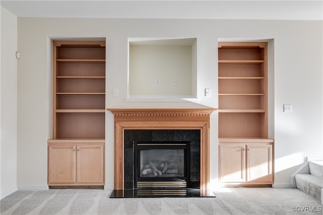 unfurnished living room with light carpet, built in shelves, and a premium fireplace