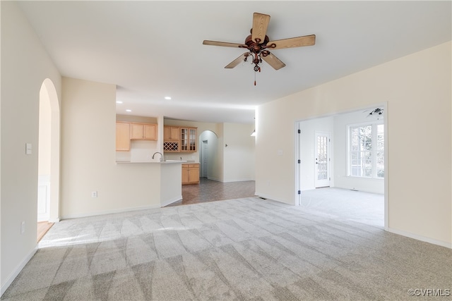 unfurnished living room featuring ceiling fan, light colored carpet, and sink