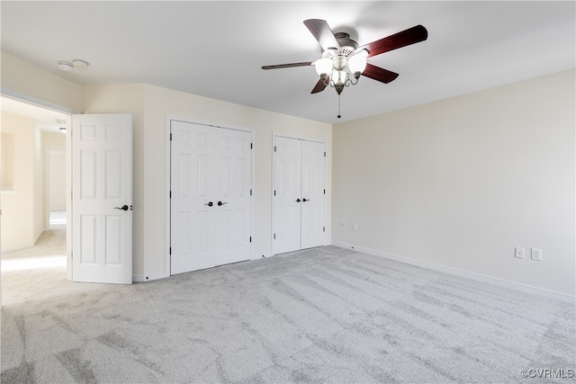 unfurnished bedroom featuring two closets, light colored carpet, and ceiling fan