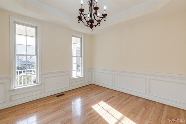 spare room featuring a tray ceiling, a healthy amount of sunlight, and an inviting chandelier