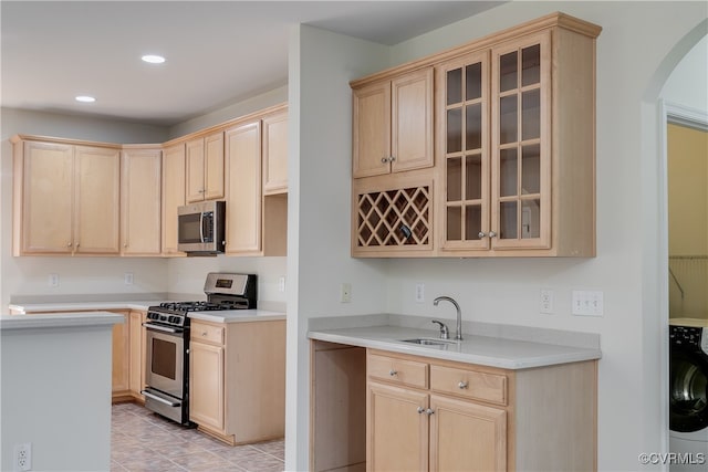 kitchen with sink, stainless steel appliances, washer / dryer, light brown cabinetry, and light tile patterned floors