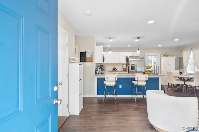 kitchen with appliances with stainless steel finishes, hanging light fixtures, white cabinetry, dark wood-type flooring, and a breakfast bar area