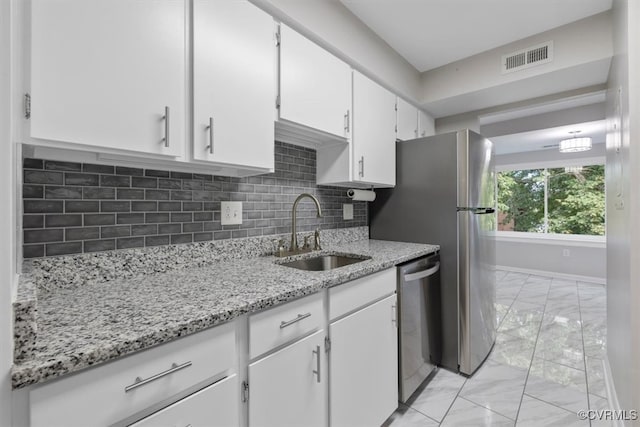 kitchen with white cabinets, backsplash, light stone countertops, dishwasher, and sink