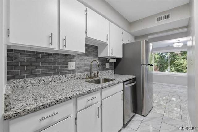 kitchen with appliances with stainless steel finishes, a sink, marble finish floor, white cabinetry, and backsplash
