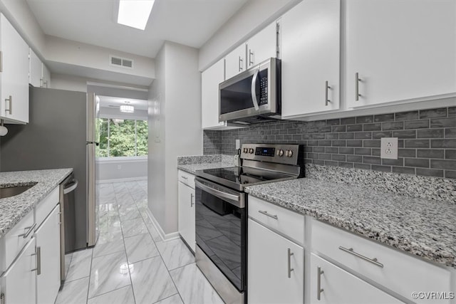 kitchen featuring appliances with stainless steel finishes, light stone counters, white cabinets, and tasteful backsplash