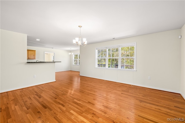 unfurnished living room featuring a notable chandelier, light hardwood / wood-style flooring, and plenty of natural light