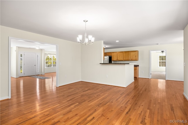 unfurnished living room featuring light wood-type flooring and ceiling fan with notable chandelier