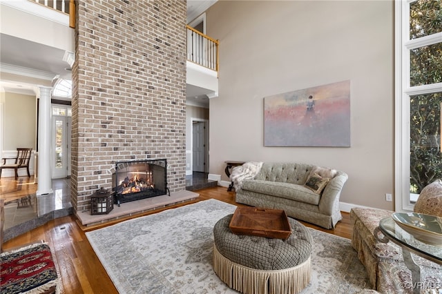 living room featuring a towering ceiling, wood-type flooring, a fireplace, and decorative columns