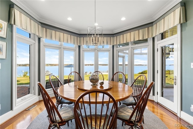 dining area featuring light hardwood / wood-style floors, ornamental molding, and a water view