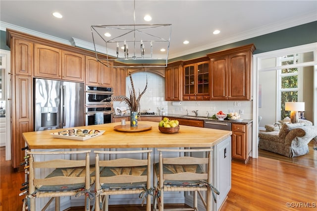 kitchen with appliances with stainless steel finishes, sink, butcher block countertops, light hardwood / wood-style floors, and crown molding