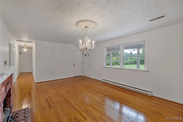 empty room featuring a textured ceiling, a fireplace, light hardwood / wood-style floors, a notable chandelier, and baseboard heating