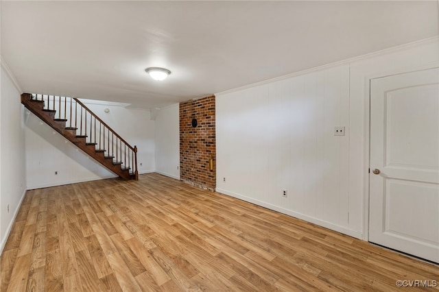 unfurnished living room with crown molding, brick wall, and light wood-type flooring