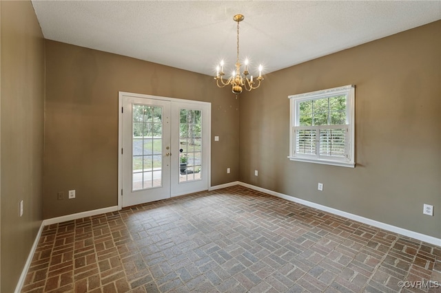 unfurnished room featuring a healthy amount of sunlight, a textured ceiling, and a chandelier