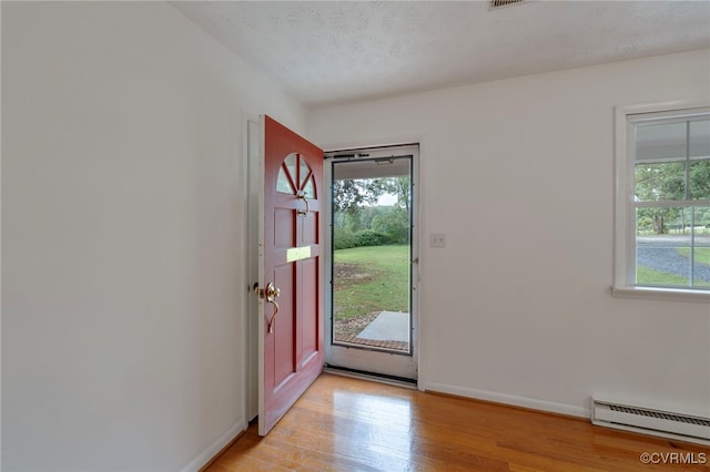 foyer entrance featuring light wood-type flooring, a textured ceiling, and baseboard heating