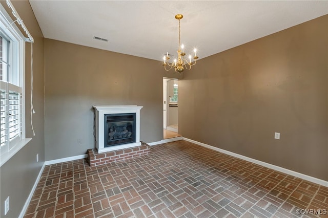 unfurnished living room featuring a chandelier and a brick fireplace