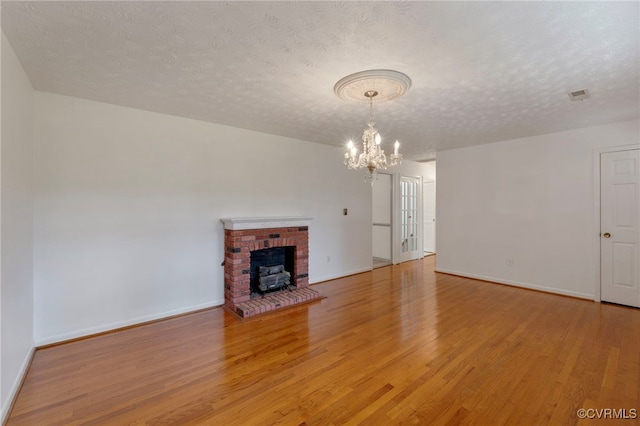 unfurnished living room with a textured ceiling, a chandelier, light wood-type flooring, and a fireplace