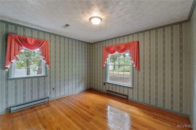 unfurnished room with baseboard heating, hardwood / wood-style floors, and plenty of natural light