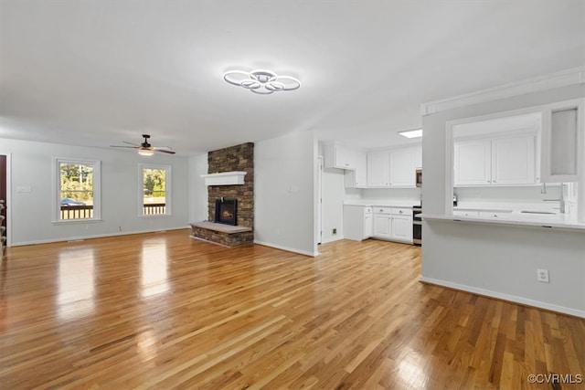 unfurnished living room with a stone fireplace, light wood-type flooring, and ceiling fan