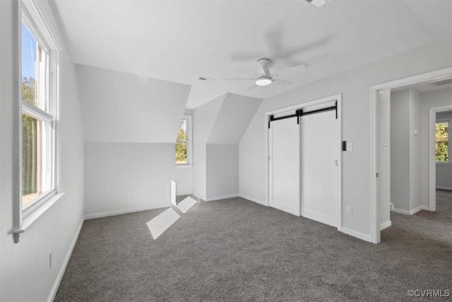 additional living space with a barn door, dark carpet, and plenty of natural light