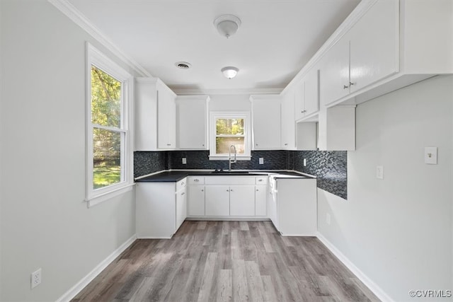 kitchen with light hardwood / wood-style floors, crown molding, white cabinets, and backsplash