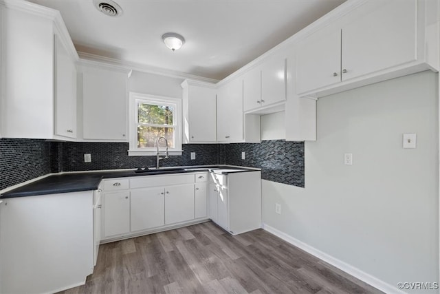 kitchen featuring white cabinets, tasteful backsplash, light wood-type flooring, ornamental molding, and sink