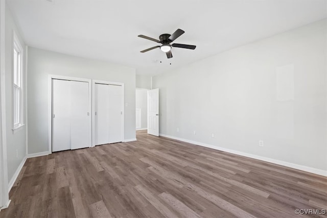 unfurnished bedroom with multiple closets, wood-type flooring, and ceiling fan