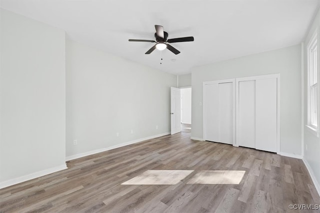 unfurnished bedroom with two closets, light wood-type flooring, and ceiling fan