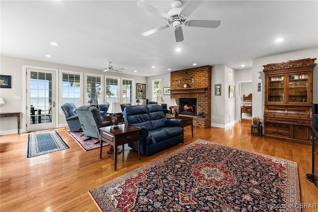 living room with a brick fireplace, light hardwood / wood-style flooring, and ceiling fan