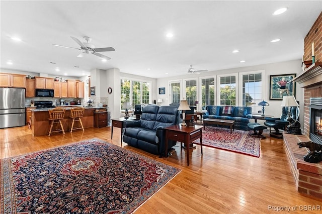 living room with ceiling fan, a fireplace, and light hardwood / wood-style flooring