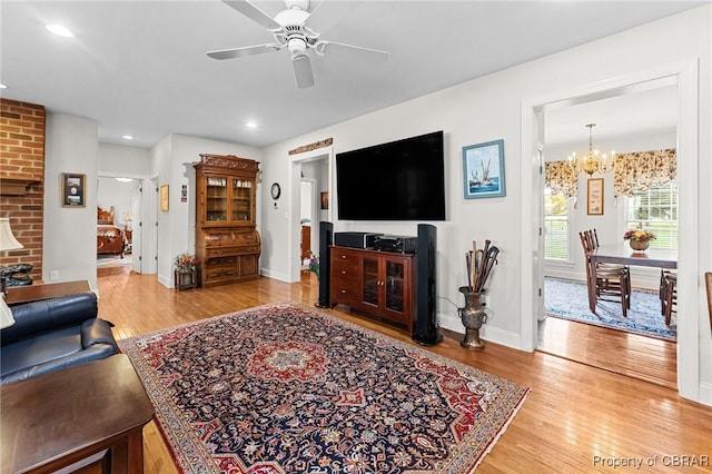 living room featuring ceiling fan with notable chandelier, wood-type flooring, and a brick fireplace