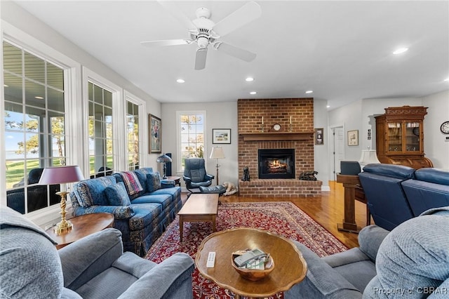 living room featuring hardwood / wood-style flooring, ceiling fan, and a brick fireplace