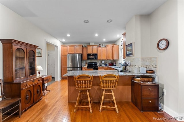 kitchen with kitchen peninsula, decorative backsplash, light wood-type flooring, and black appliances