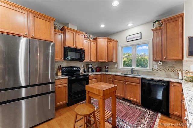 kitchen with backsplash, black appliances, sink, light stone countertops, and light wood-type flooring