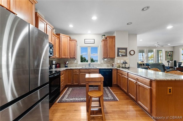 kitchen featuring kitchen peninsula, a wealth of natural light, black appliances, and light wood-type flooring